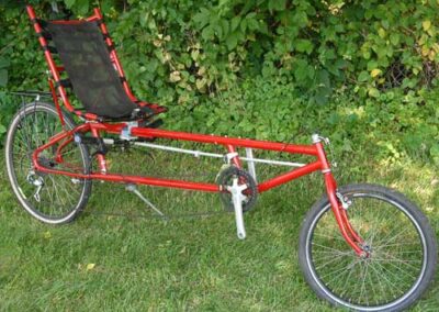 A red bicycle with a black seat parked in the grass.