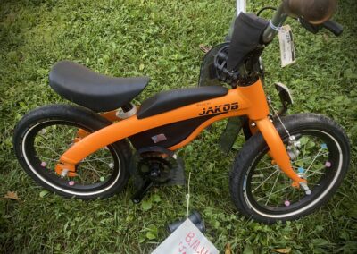 A small orange bike with a tag on it.